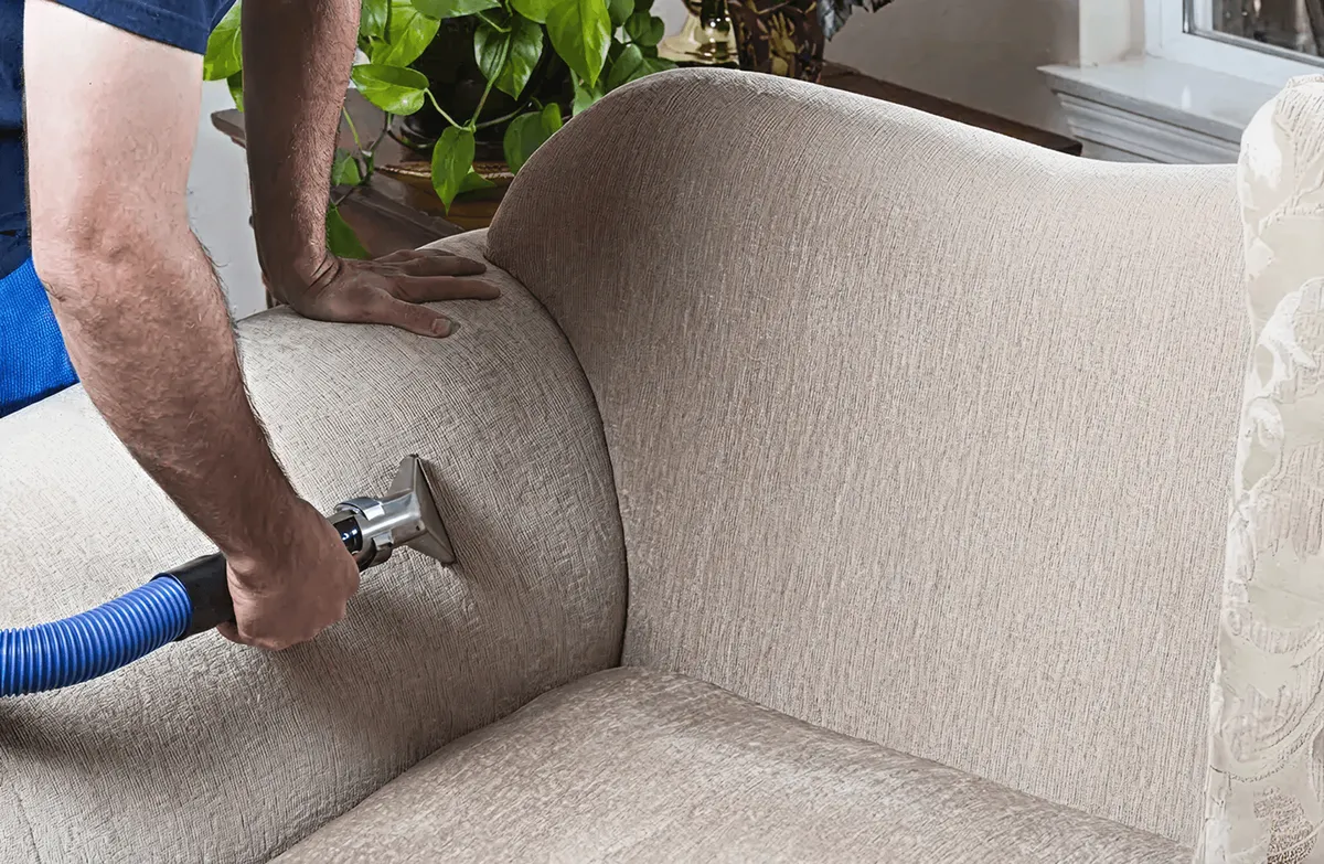 Professional upholstery cleaner deep-cleaning a fabric sofa with a handheld extraction tool and hose, Pasadena, CA.